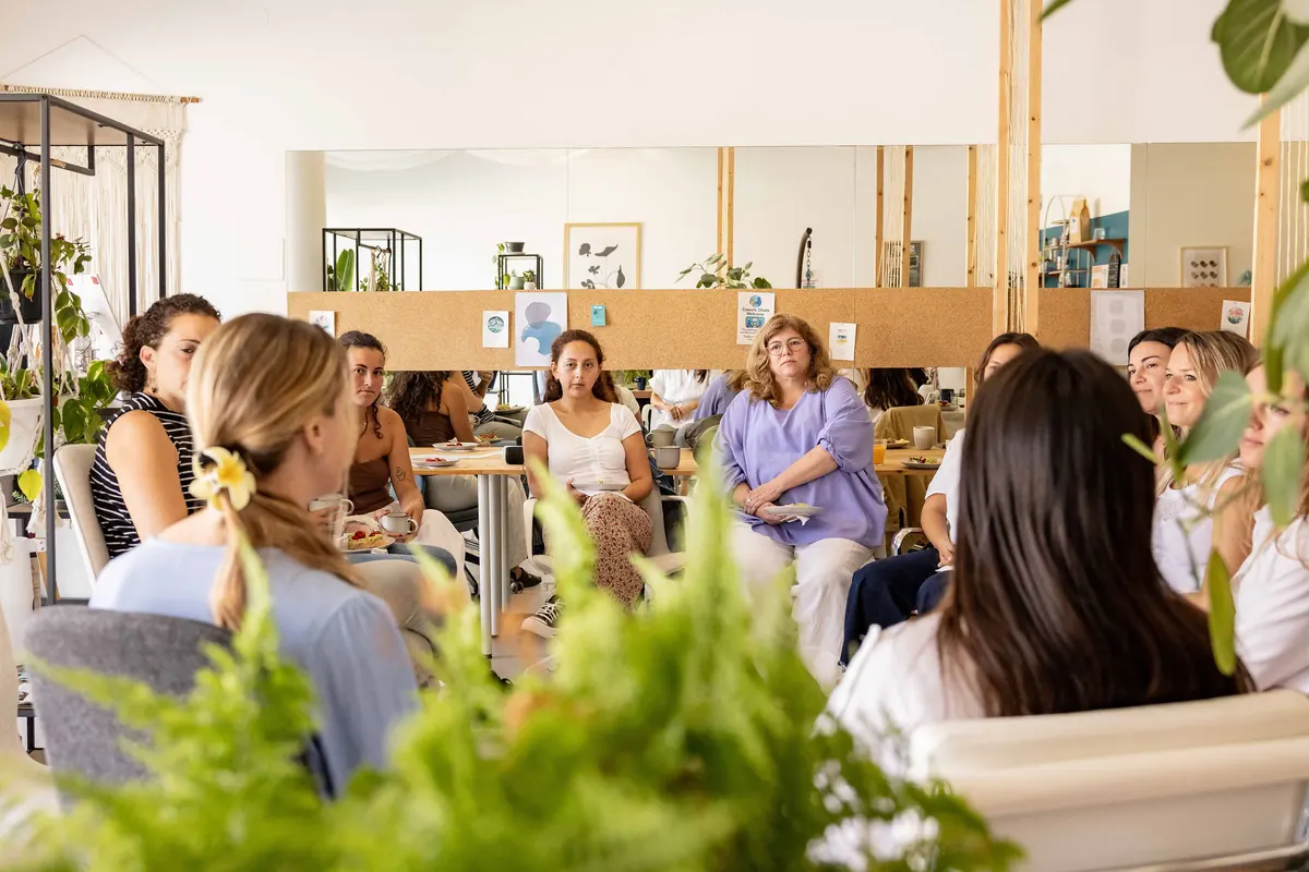 A circle of guests seated in a bright, plant-filled room